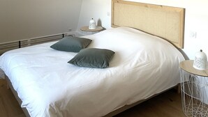 A neatly made bed with two pillows, a bedside table with a lamp, and a small round table with a decorative item. - Apartment Cypress (Stutzheim-Offenheim)
