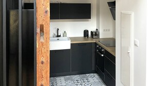 A modern kitchen with black cabinets, a wooden beam ceiling, and a patterned tile floor. - Apartment Cypress (Stutzheim-Offenheim)
