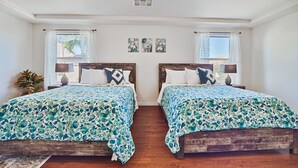 Una habitación con dos camas de madera, cada una con un edredón estampado con motivos florales, una mesita de noche con una lámpara y una ventana con cortinas de diseño.