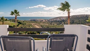 A balcony with two chairs facing a coastal view, palm trees, and a distant town. - Belvilla by OYO Vistalmar (Manilva, Malaga)