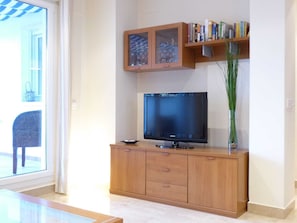 Een woonkamer met een houten tv-meubel, een flatscreen televisie, een boekenkast en uitzicht door een glazen deur.