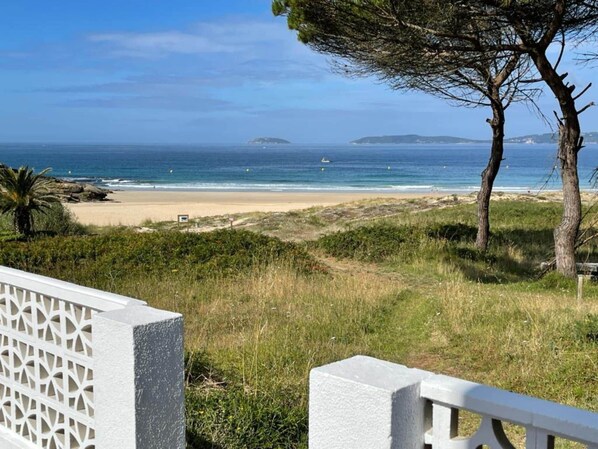 A coastal landscape with a beach, grassy terrain, and a clear view of the ocean.