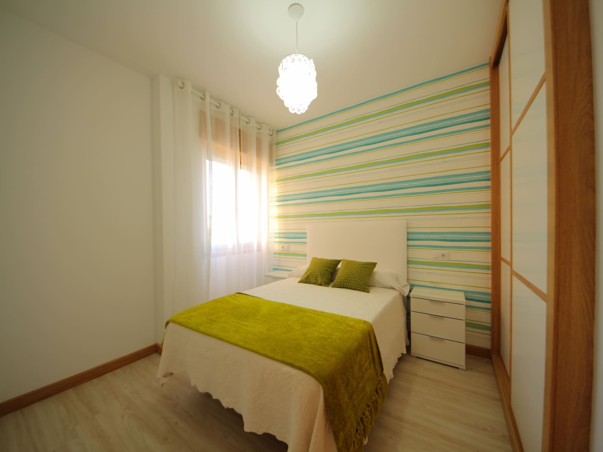 A bedroom with a bed, a bedside table, a dresser, and a window with curtains.