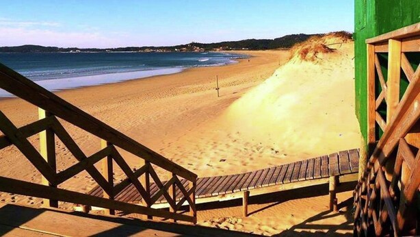A beach with a wooden staircase leading to a green building. - Villa in Vilamoura near Golf & Beach (Sanxenxo)