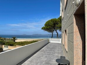 A balcony with a view of the sea, a tree, and a building with a stone facade.