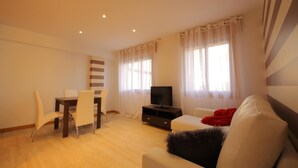 A modern living room with a sofa, a TV, a dining table with chairs, and a window with curtains. - Villa in Vilamoura near Golf & Beach (Sanxenxo)