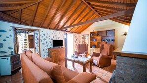 Una sala de estar acogedora con una pared de piedra, vigas de madera en el techo, un televisor y una chimenea.