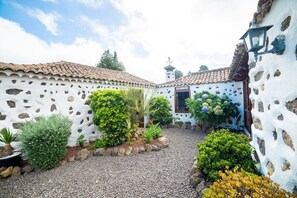 Un patio con paredes blancas, techo de tejas y un sendero de grava.