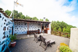 Un patio con una mesa y sillas, un banco de madera, una planta en maceta y un edificio rústico con tejado de tejas.