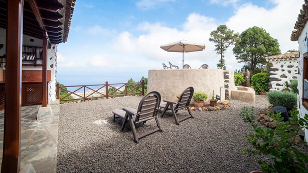 Un área de estar al aire libre con dos sillas, una mesa, un muro de piedra y vista al mar.