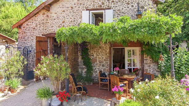 A stone house with a garden, outdoor seating, and a rustic aesthetic.