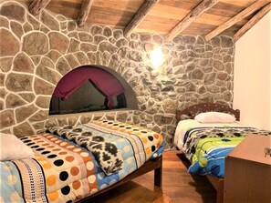 Un dormitorio con dos camas, paredes de piedra, vigas de madera y una chimenea de piedra.