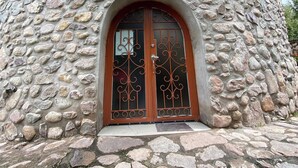 Un bâtiment en pierre, doté d’un toit en bois et d’une entrée centrale en arc surmontée d’une décoration en métal.