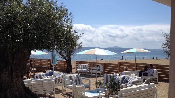A beachside seating area with white furniture and umbrellas, overlooking the sea. - Luxury villa with heated jacuzzi and garden (Le Muy)