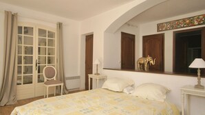 A bedroom with a bed, a chair, a small table, a mirror, and a door with curtains. - Luxury villa with heated jacuzzi and garden (Le Muy)