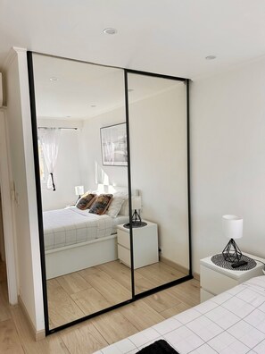 A modern bedroom with a large mirror wardrobe, a bedside table with a lamp, and a bed with patterned bedding.