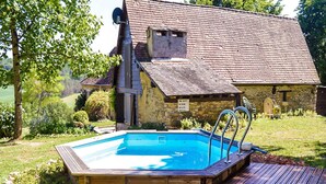 A wooden swimming pool with a deck, surrounded by a stone building with a sloped roof. - Rustic Chic Country Cottage (Thenon)