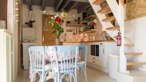 A kitchen with a dining area, featuring a table with chairs, a refrigerator, an oven, and a staircase. - Rustic Chic Country Cottage (Thenon)