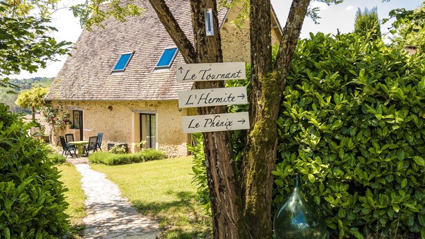 A rustic building with a stone facade, a sloped roof, and a pathway leading to a table and chairs set outside. - Rustic Chic Country Cottage (Thenon)