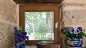 A stone wall with a wooden door and window, two potted plants with purple flowers, and a small wooden chest. - Rustic Chic Country Cottage (Thenon)