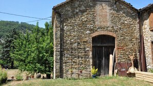 Un bâtiment en pierre doté d’une grande porte en arc de cercle, entouré de verdure et d’arbres.