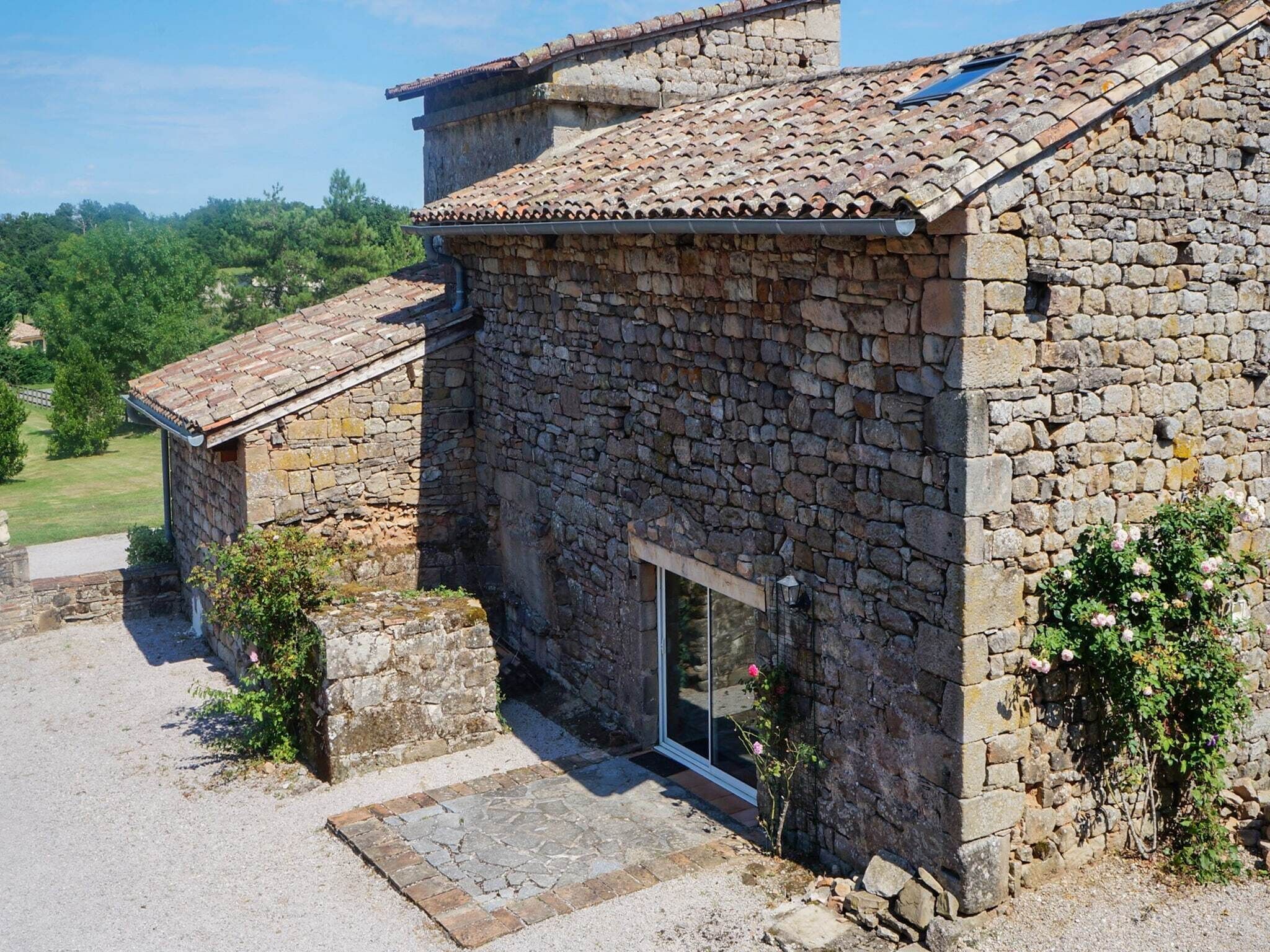 Un edificio de piedra con tejado de tejas, puerta de cristal y un pequeño jardín con plantas.
