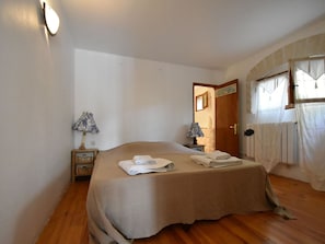 Un dormitorio con una cama, dos lámparas de noche, suelo de madera y una puerta que da a otra habitación.
