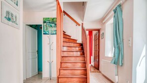 Eine Treppe mit Holzbodenstufen führt zu einer Zwischenplattform, einem Kleiderständer und einer Tür mit rotem Rahmen.