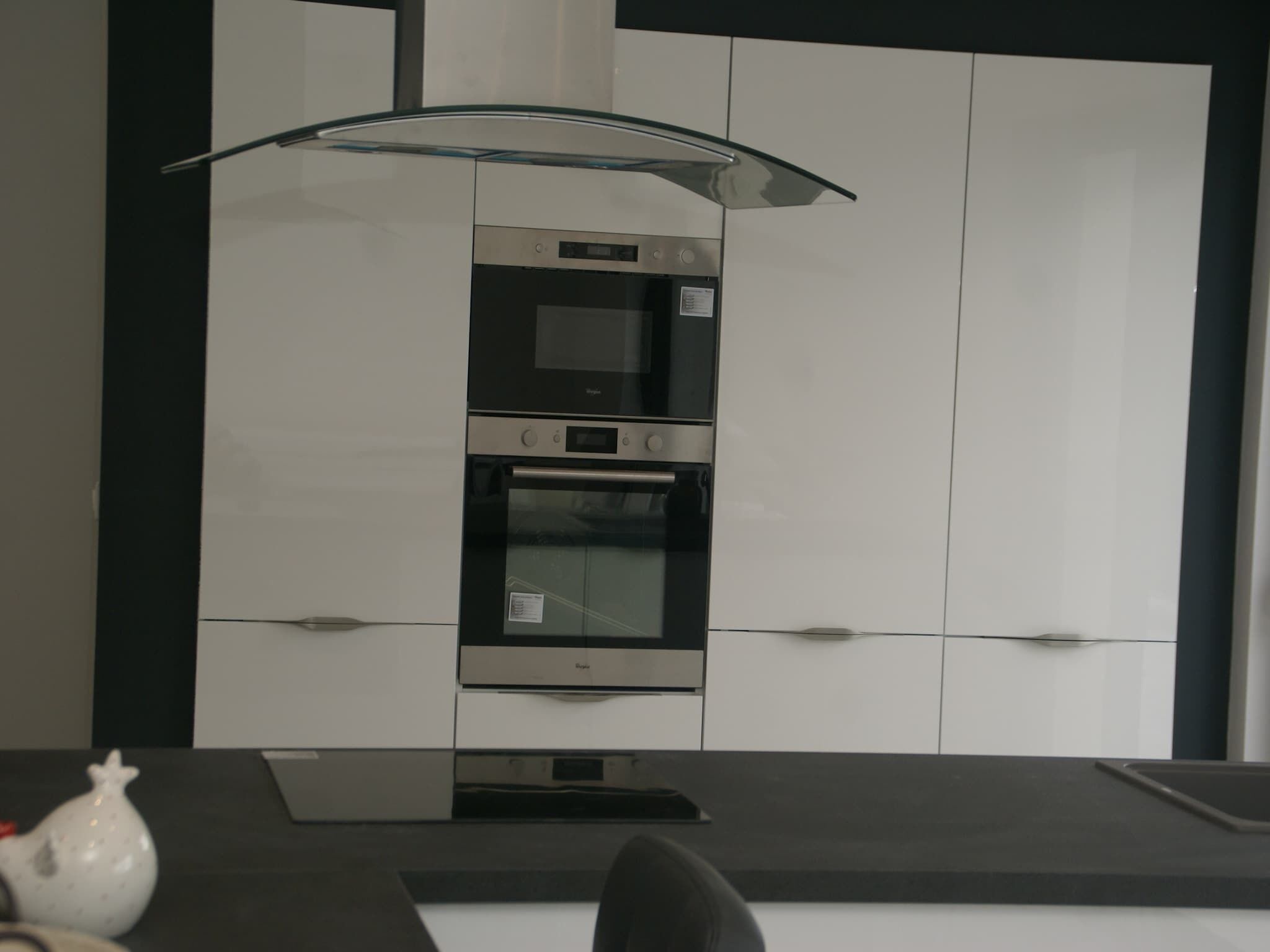 A modern kitchen with a built-in oven, microwave, and a glass-fronted range hood.