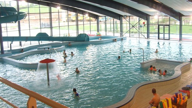 Una piscina interior con múltiples carriles, una zona de clavados y un área de descanso con vistas al exterior.
