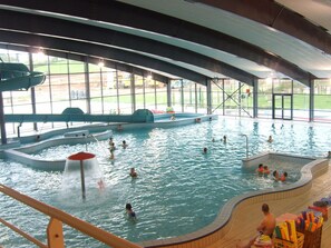 An indoor swimming pool with multiple lanes, a diving area, and a seating area with a view of the outdoors.