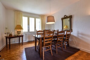 Un comedor con una mesa y sillas de madera, una lámpara, un espejo y un ventanal con cortinas.