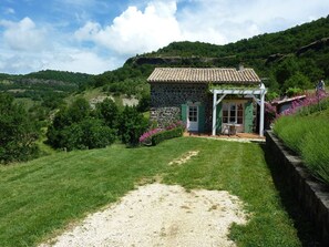 Uma casa de pedra com telhado de telhas, um pequeno alpendre e um caminho de cascalho que leva à entrada.