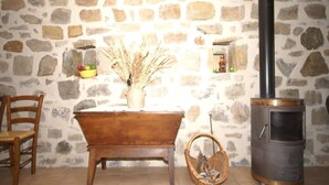 A rustic room with a stone wall, a wooden bathtub, a wicker basket, and a wood-burning stove.