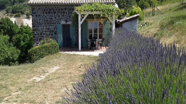 A stone house with a covered patio and a lavender field in the foreground.