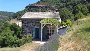 A stone house with a tiled roof, a covered porch, and a garden with lavender.