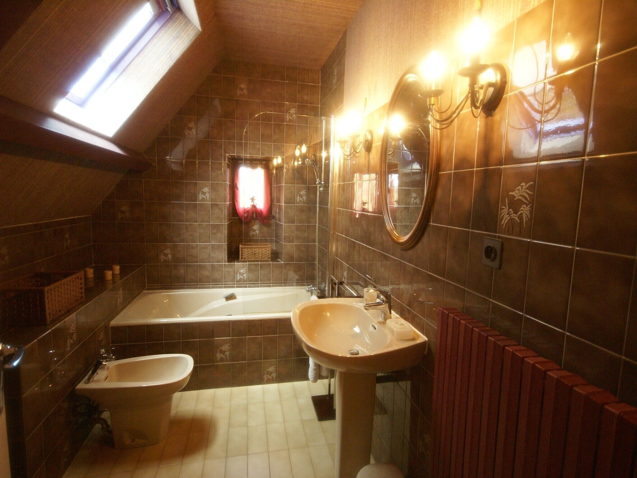 A bathroom with a bathtub, a sink, and a toilet. There is a skylight above the bathtub, and the walls are tiled with a pattern.