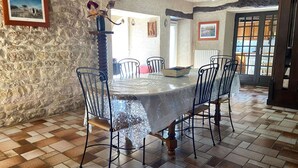Un espace repas avec un mur en pierre, un sol carrelé et une table ronde entourée de chaises.