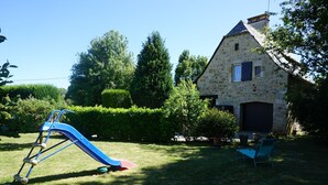 Une maison en pierre avec un toboggan bleu dans une cour verdoyante.