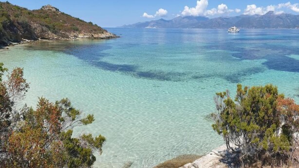 A coastal landscape with clear turquoise waters, a boat in the distance, and a mountainous backdrop. - Riverside Home in Folelli (Folelli)