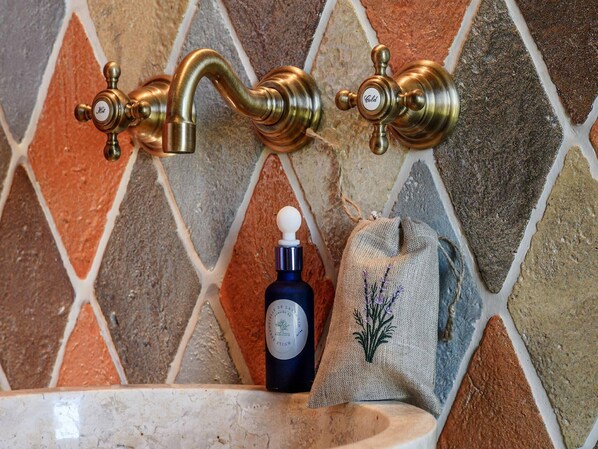 Un baño con un revestimiento de mosaicos de piedra, un lavamanos y una botella de jabón.