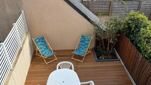 A patio with a white table and two blue-patterned lounge chairs. - Cottage (Guidel)