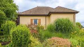 A house with a tiled roof, surrounded by a variety of plants and flowers. - Pleasant holiday home with private pool (St Nexans)