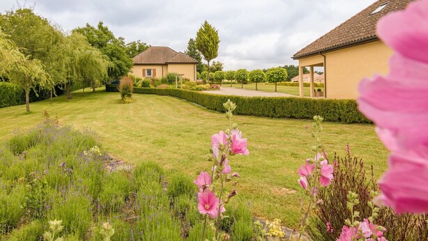 A residential area with two houses, a well-maintained lawn, and a variety of flowering plants. - Pleasant holiday home with private pool (St Nexans)