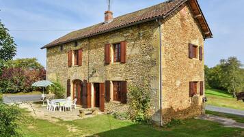 A stone house with a tiled roof, a chimney, and a small patio with a table and chairs.