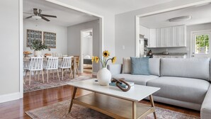 A modern living room with a white sofa, a coffee table, and a dining area with white chairs and a patterned rug.