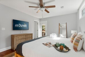 A hotel room with a bed, a television, a ceiling fan, a wooden dresser, and a window.