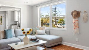 A modern living room with a gray sectional sofa, a white coffee table, and a large window with a view of the street.