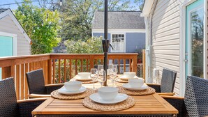 A wooden deck with a table set for dining, surrounded by wicker chairs.