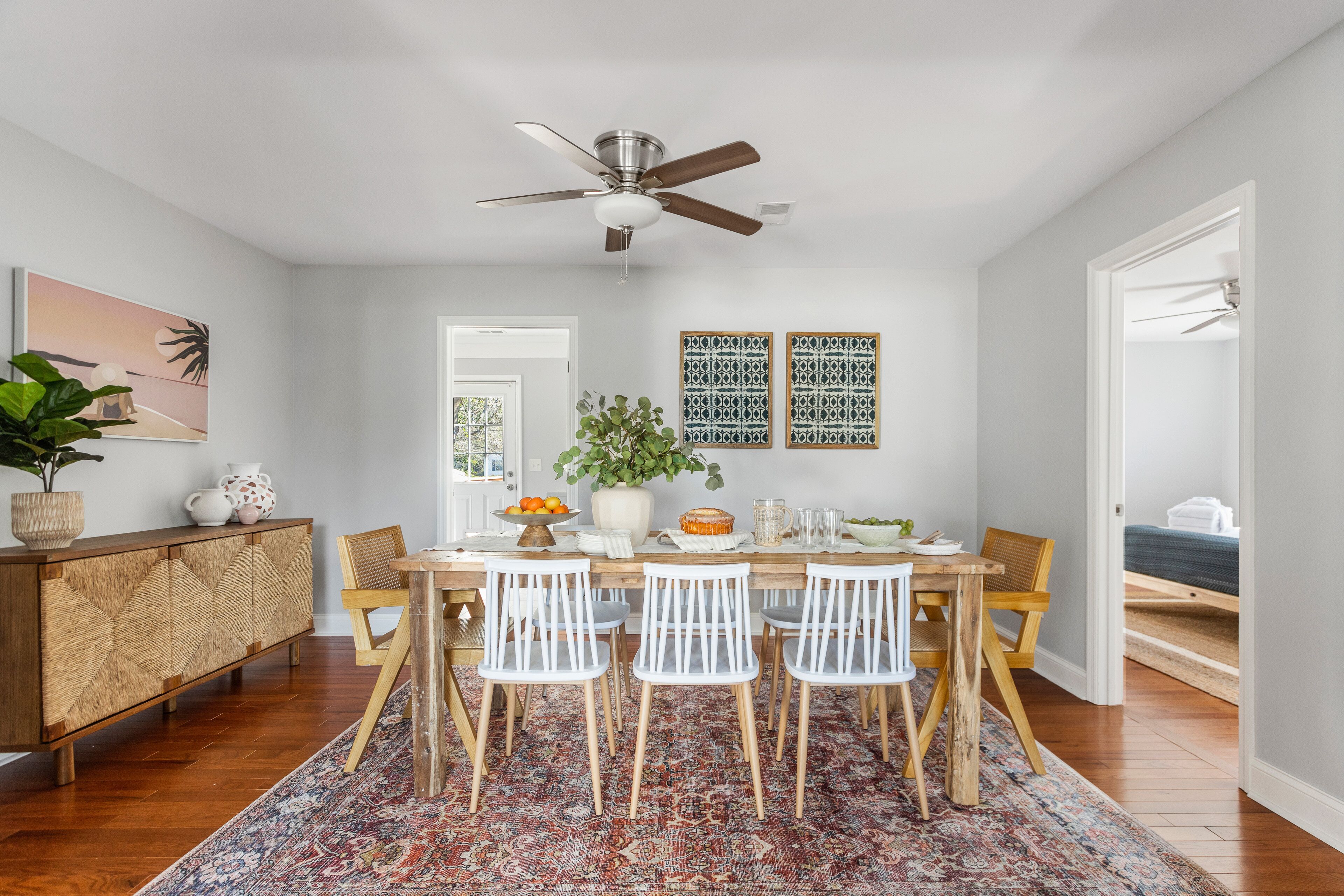 A dining area with a wooden table, white chairs, a ceiling fan, and a patterned rug.